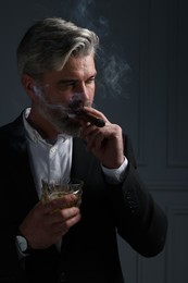 Handsome bearded man with glass of whiskey smoking cigar against dark grey background