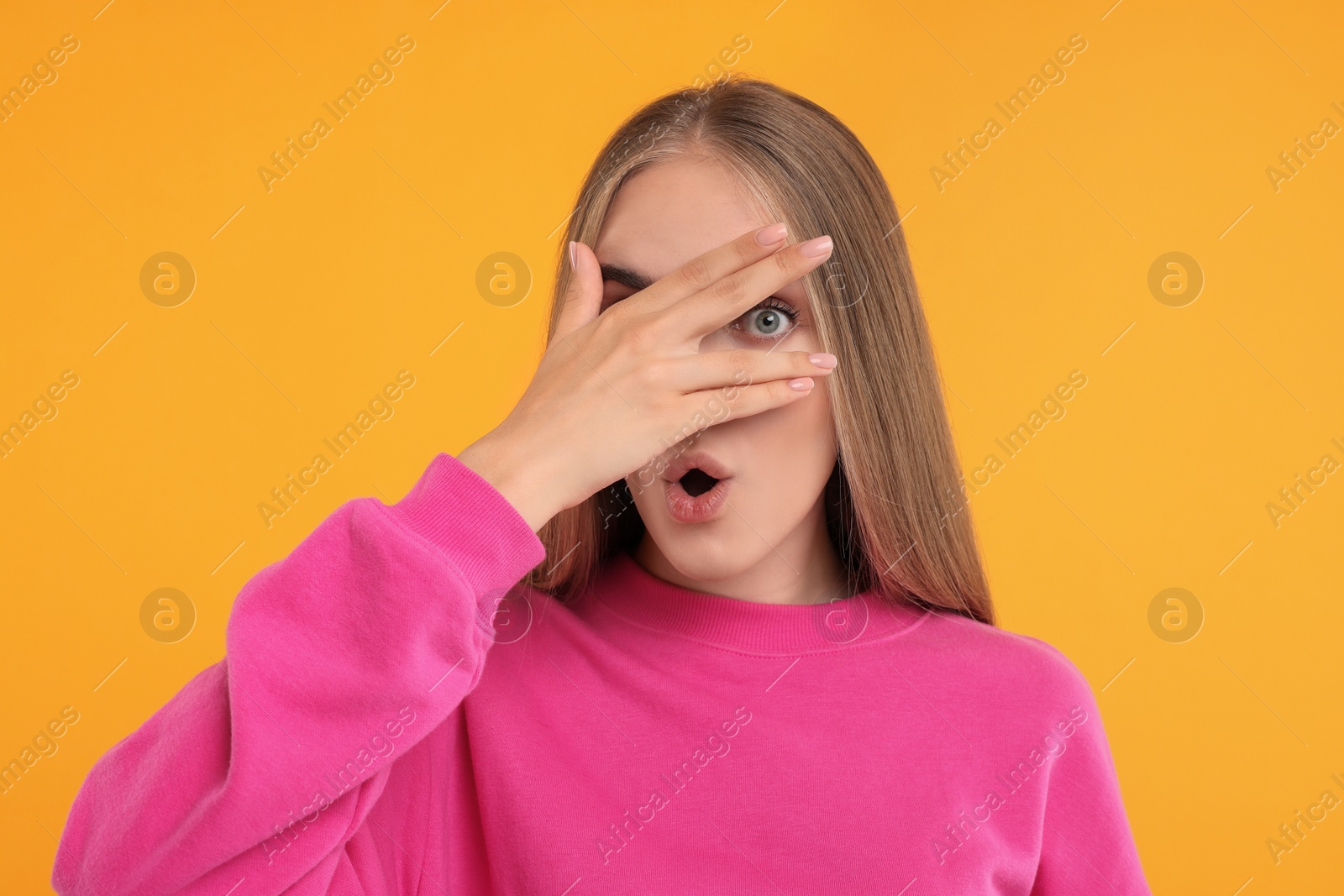 Photo of Embarrassed woman covering face with hand on orange background