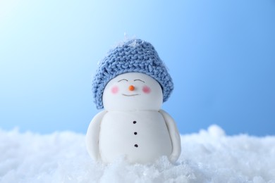 Photo of Cute decorative snowman on artificial snow against light blue background, closeup