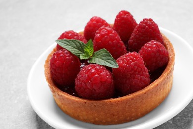 Photo of Tartlet with fresh raspberries and mint on light grey table. Delicious dessert