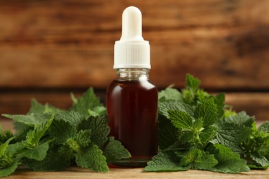 Photo of Glass bottle of nettle oil with dropper and leaves on wooden table, closeup