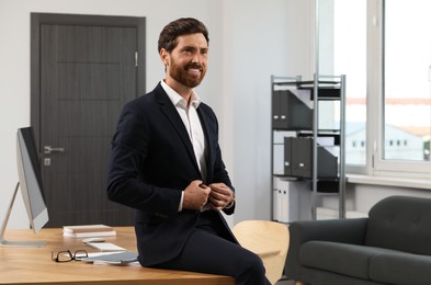 Photo of Smiling bearded man sitting on table in office