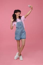 Photo of Beautiful young woman taking selfie on pink background