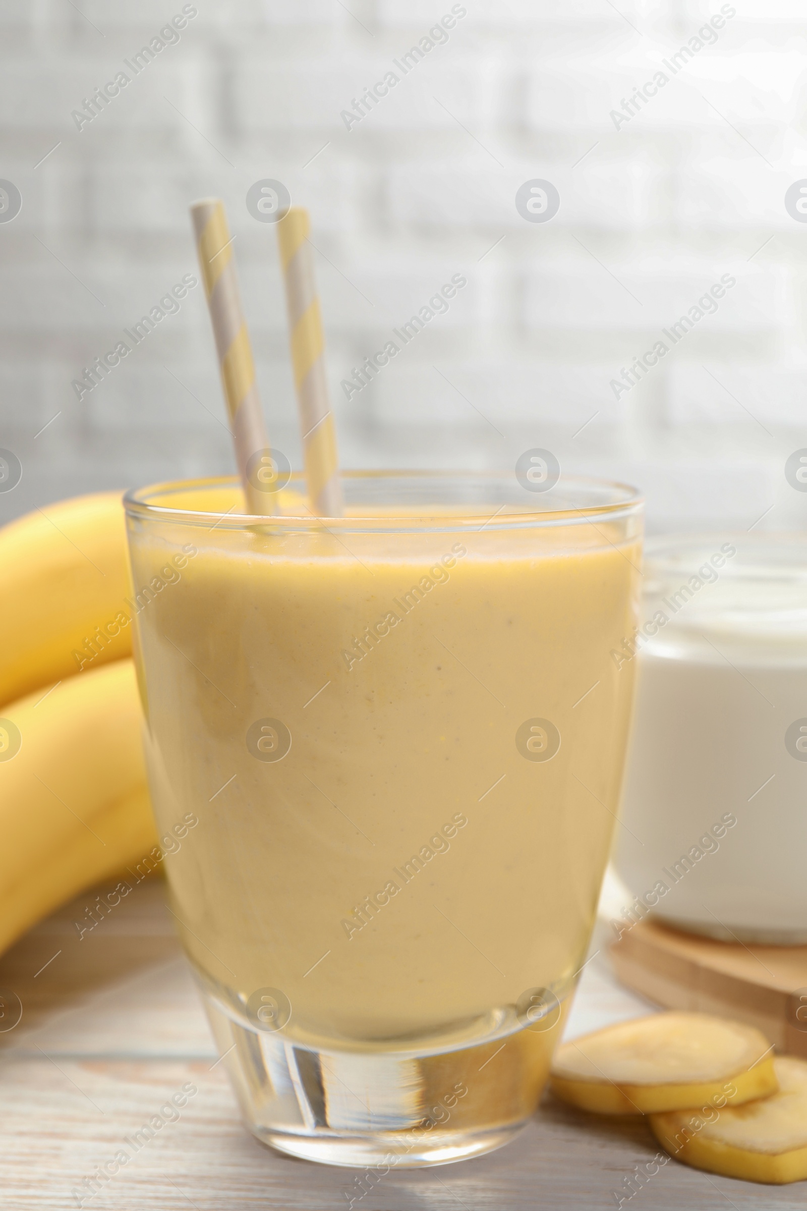 Photo of Glass of tasty banana smoothie with straws and ingredients on white wooden table