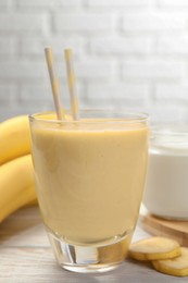 Photo of Glass of tasty banana smoothie with straws and ingredients on white wooden table