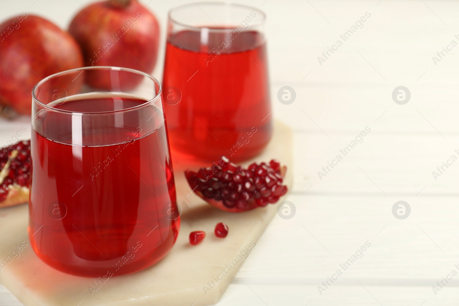 Photo of Tasty pomegranate juice in glasses and fresh fruits on white wooden table, closeup. Space for text