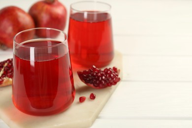 Photo of Tasty pomegranate juice in glasses and fresh fruits on white wooden table, closeup. Space for text