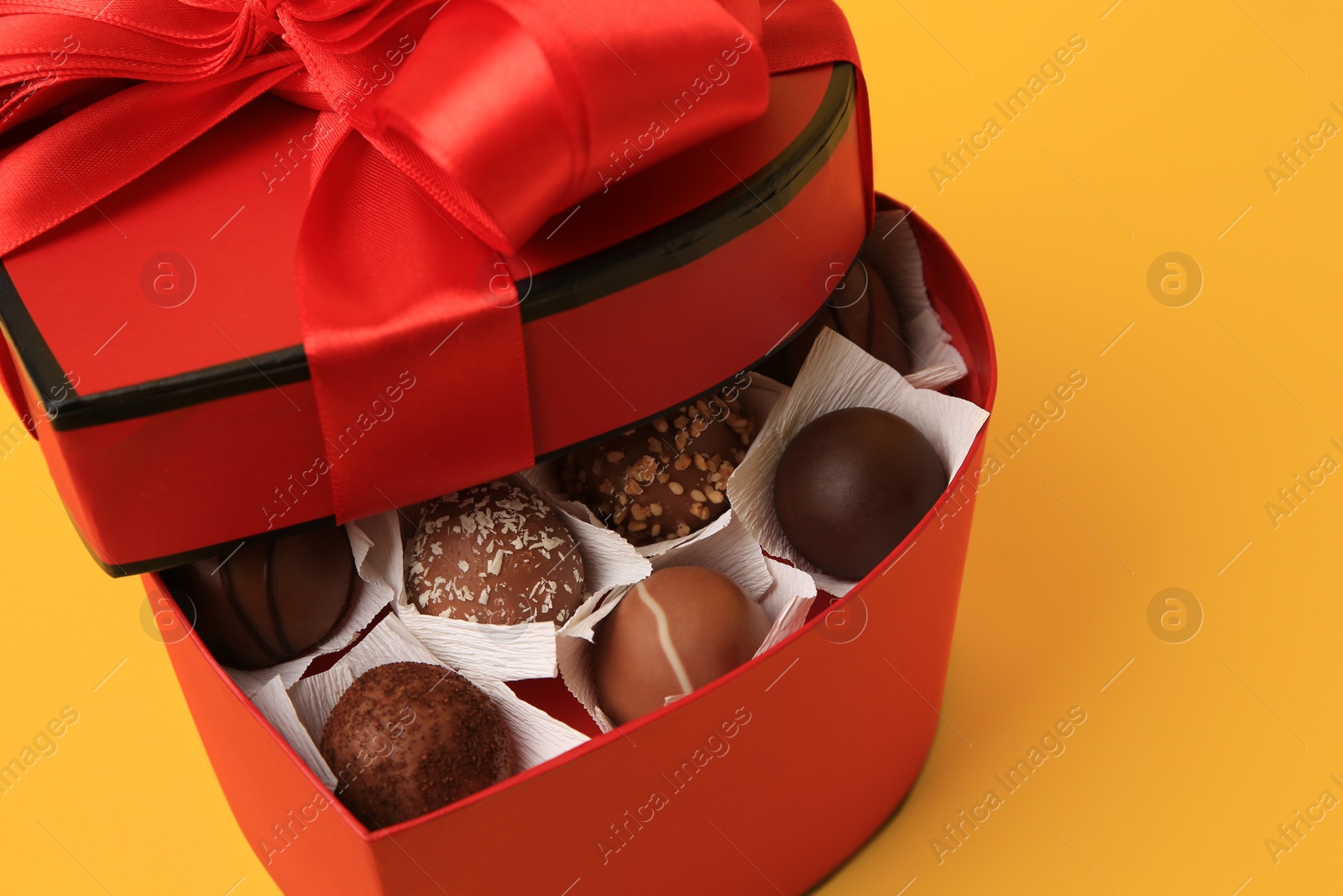 Photo of Heart shaped box with delicious chocolate candies on yellow background, closeup