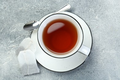 Photo of Aromatic tea in cup, teabags and spoon on grey table, top view