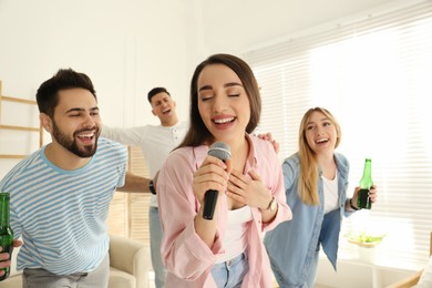 Photo of Young woman singing karaoke with friends at home