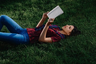 Photo of Young woman reading book while lying on green grass outdoors