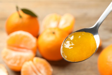 Photo of Teaspoon with tasty tangerine jam over table, closeup. Space for text