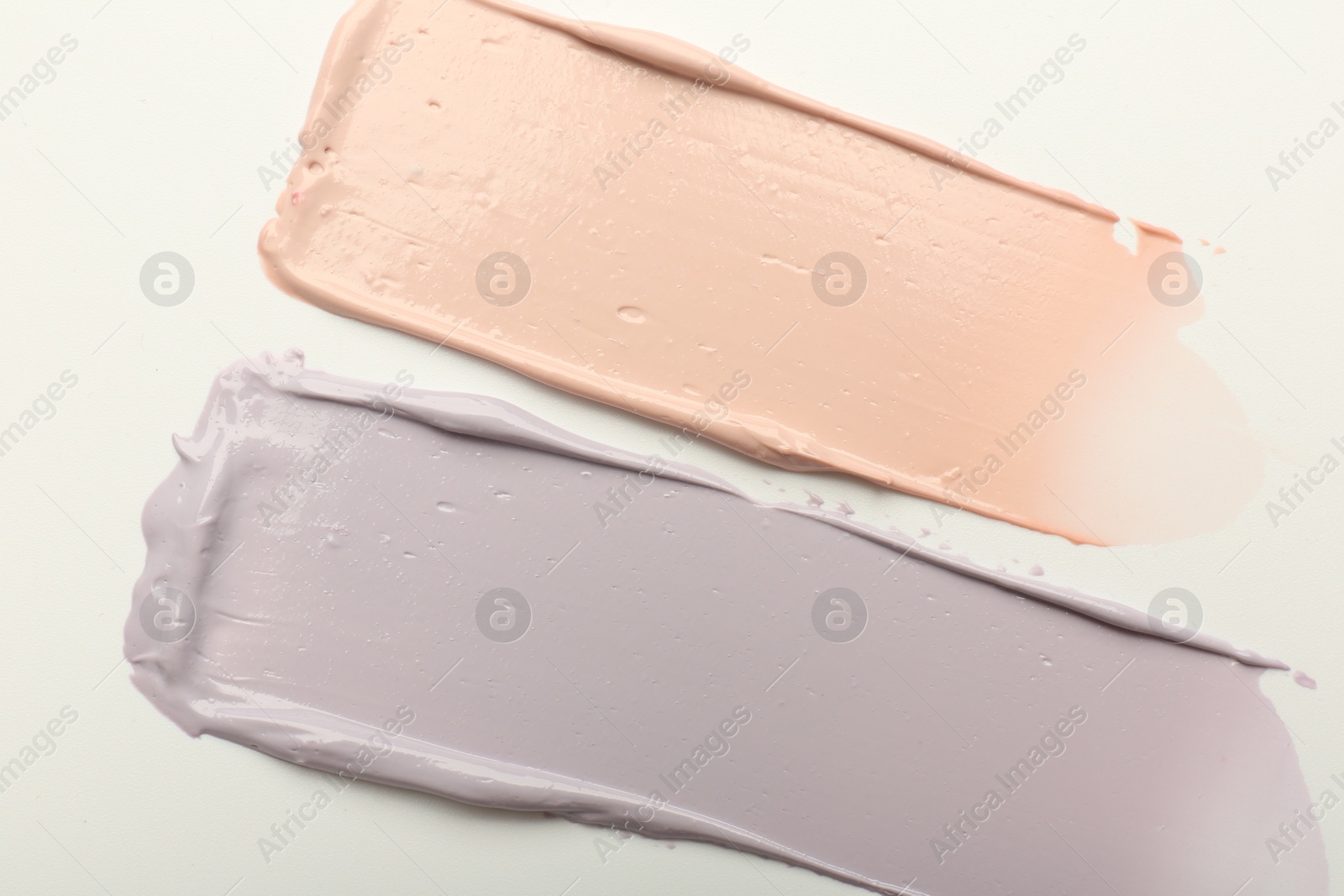 Photo of Strokes of pink and purple color correcting concealers on white background, top view