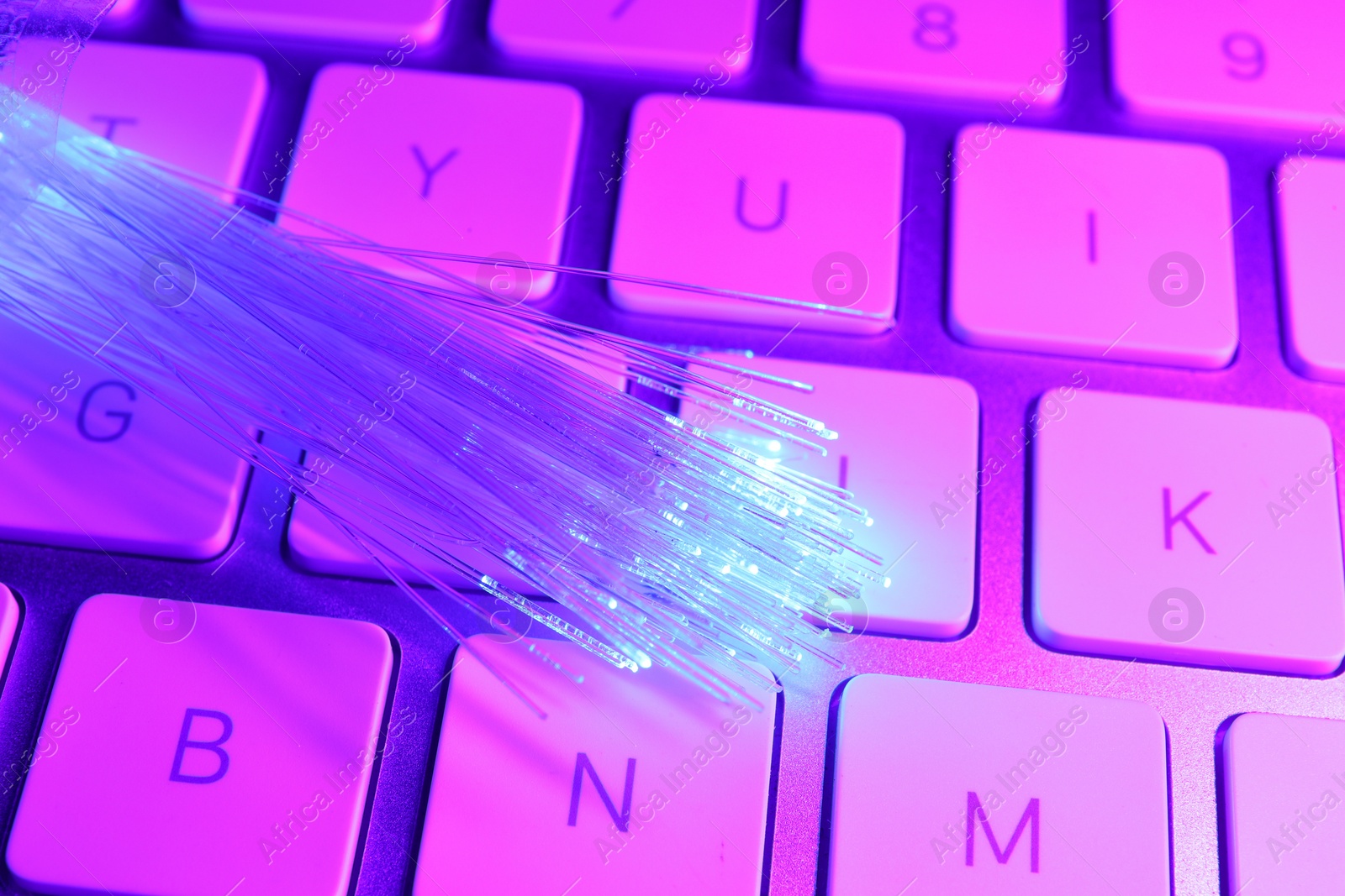 Photo of Optical fiber strands transmitting color light on computer keyboard, closeup