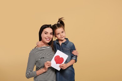 Happy woman with her cute daughter and handmade greeting card on beige background, space for text. Mother's day celebration