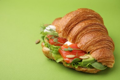 Photo of Tasty croissant with salmon, avocado, mozzarella and lettuce on green background, closeup. Space for text