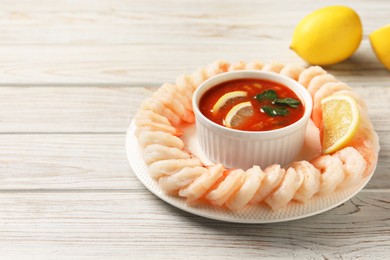 Photo of Tasty boiled shrimps with cocktail sauce and lemon on white wooden table, space for text