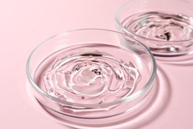 Petri dishes with liquids on pale pink background, closeup