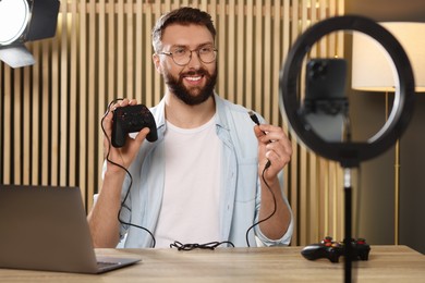 Smiling technology blogger with game controller recording video review at home