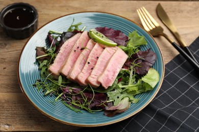 Pieces of delicious tuna steak with salad served on wooden table, closeup