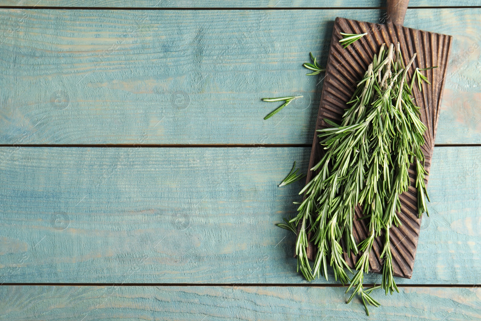 Photo of Board with fresh rosemary twigs on wooden table, top view. Space for text