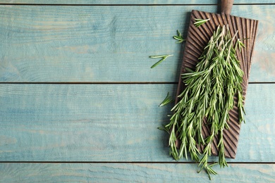 Photo of Board with fresh rosemary twigs on wooden table, top view. Space for text