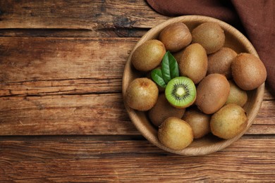 Photo of Bowl with cut and whole fresh kiwis on wooden table, flat lay. Space for text