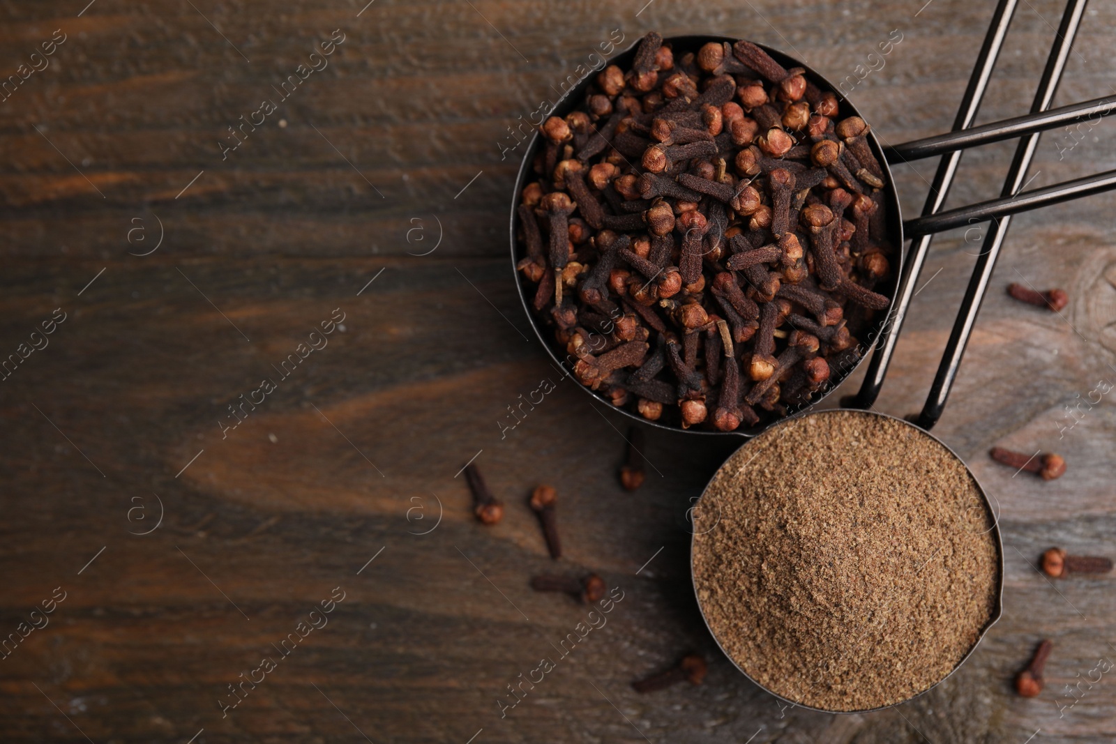 Photo of Aromatic clove powder and dried buds in scoops on wooden table, top view. Space for text