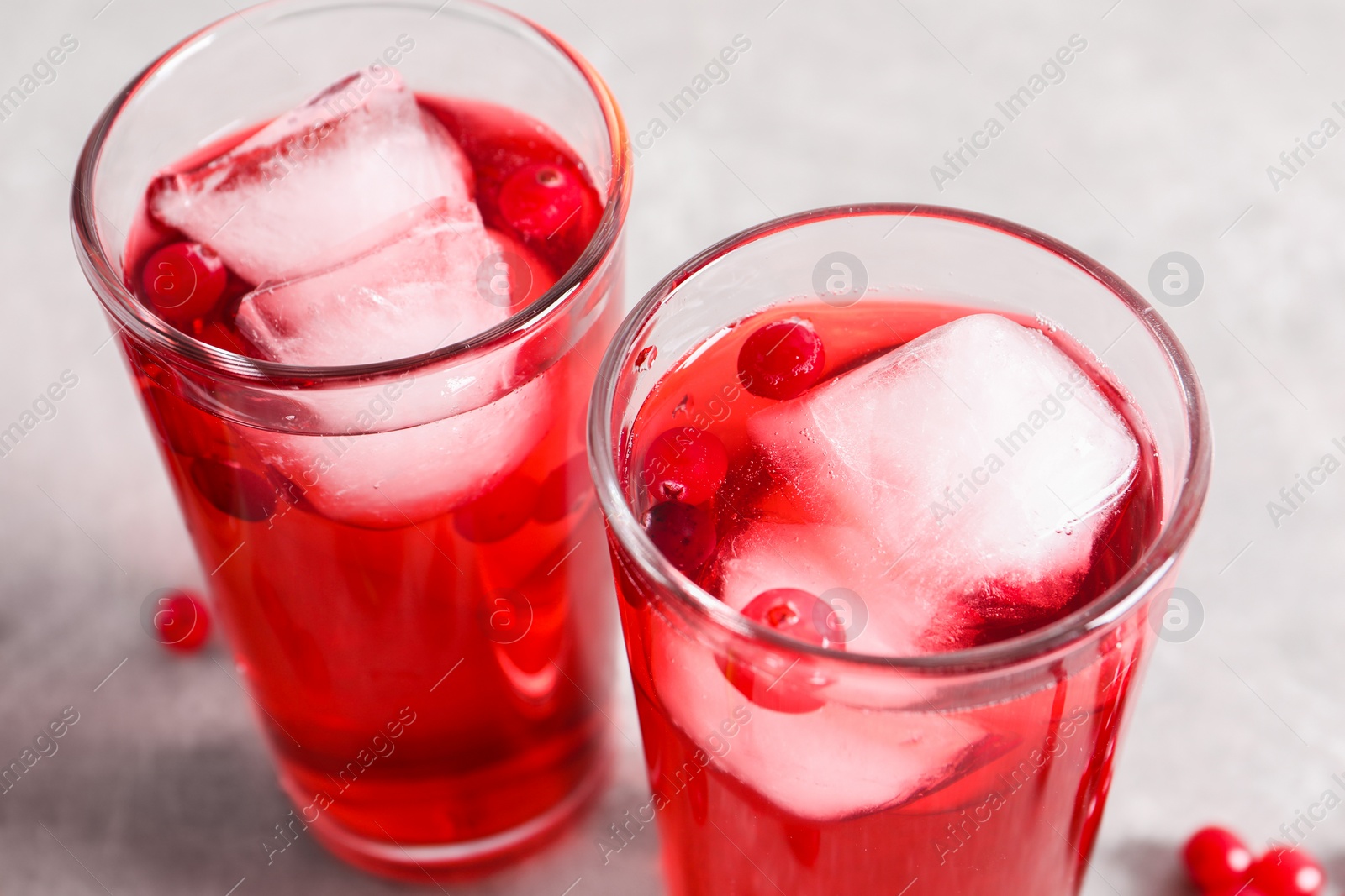 Photo of Tasty cranberry juice with ice cubes in glasses and fresh berries on light grey table, closeup