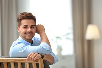 Photo of Portrait of handsome young man sitting on chair in room. Space for text