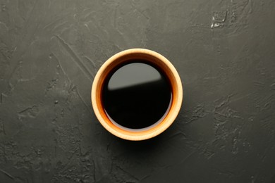 Soy sauce in wooden bowl on black textured table, top view