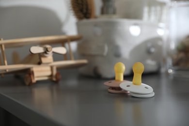 Pacifiers on grey table in child room, space for text