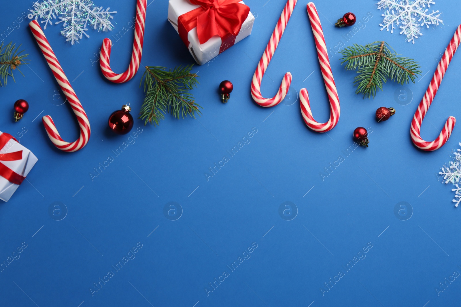 Photo of Flat lay composition with candy canes and Christmas decor on blue background. Space for text