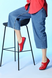 Fashionable woman in stylish shoes with stool against color background