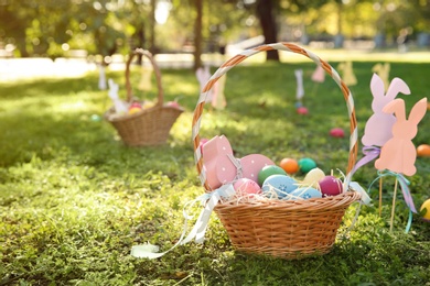 Photo of Basket with Easter eggs and decor on grass in park. Space for text