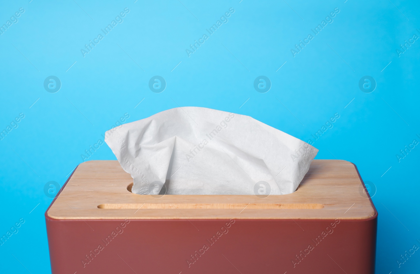 Photo of Holder with paper tissues on light blue background, closeup