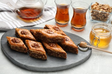 Photo of Delicious baklava with walnuts, honey and hot tea on light grey marble table