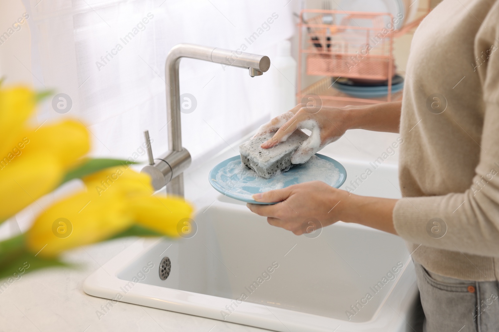 Photo of Woman washing plate above sink in modern kitchen, closeup