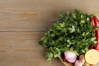 Bowl with fresh green parsley, chili peppers, lemon, onion and garlic on wooden table, top view. Space for text