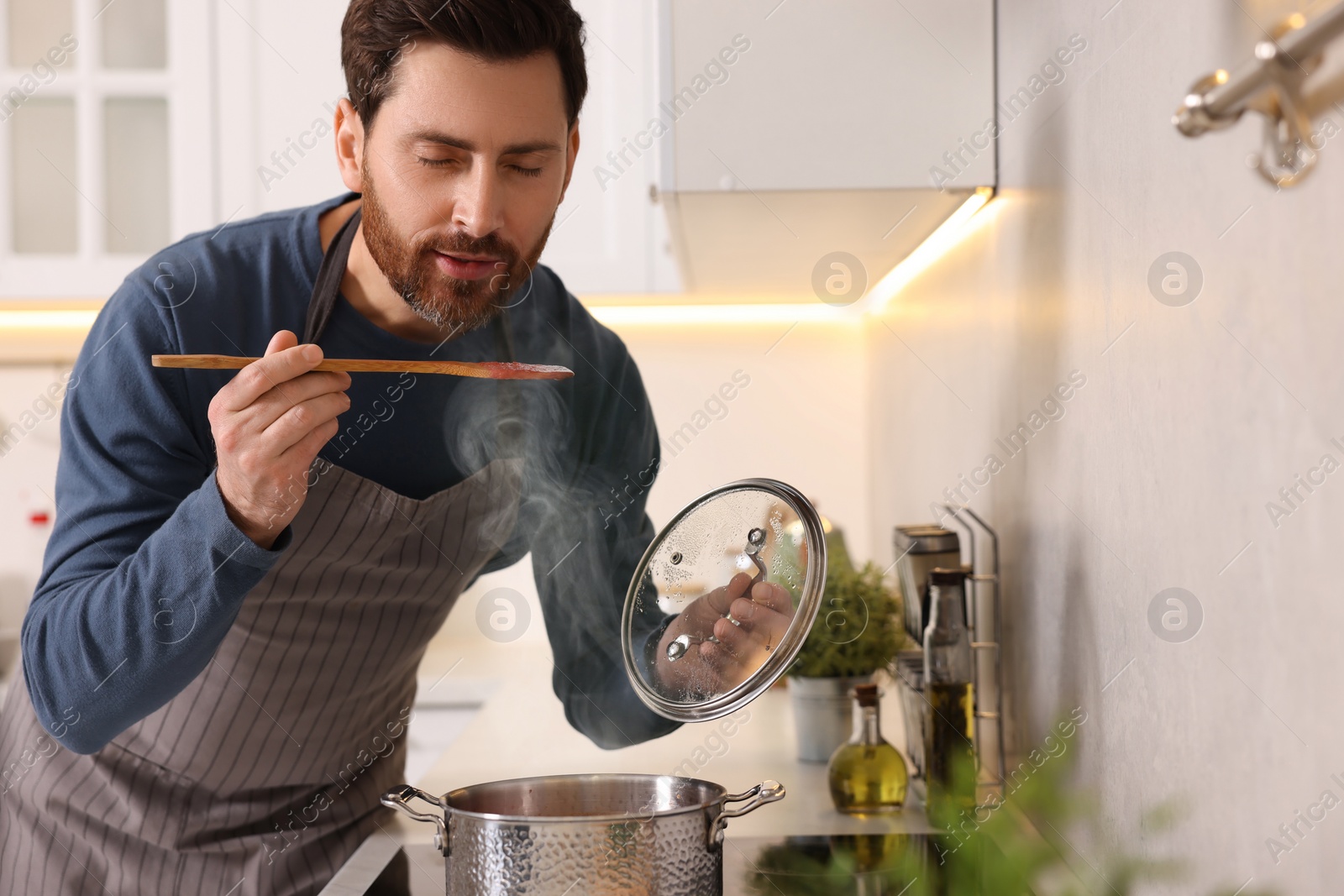 Photo of Man tasting delicious tomato soup in kitchen