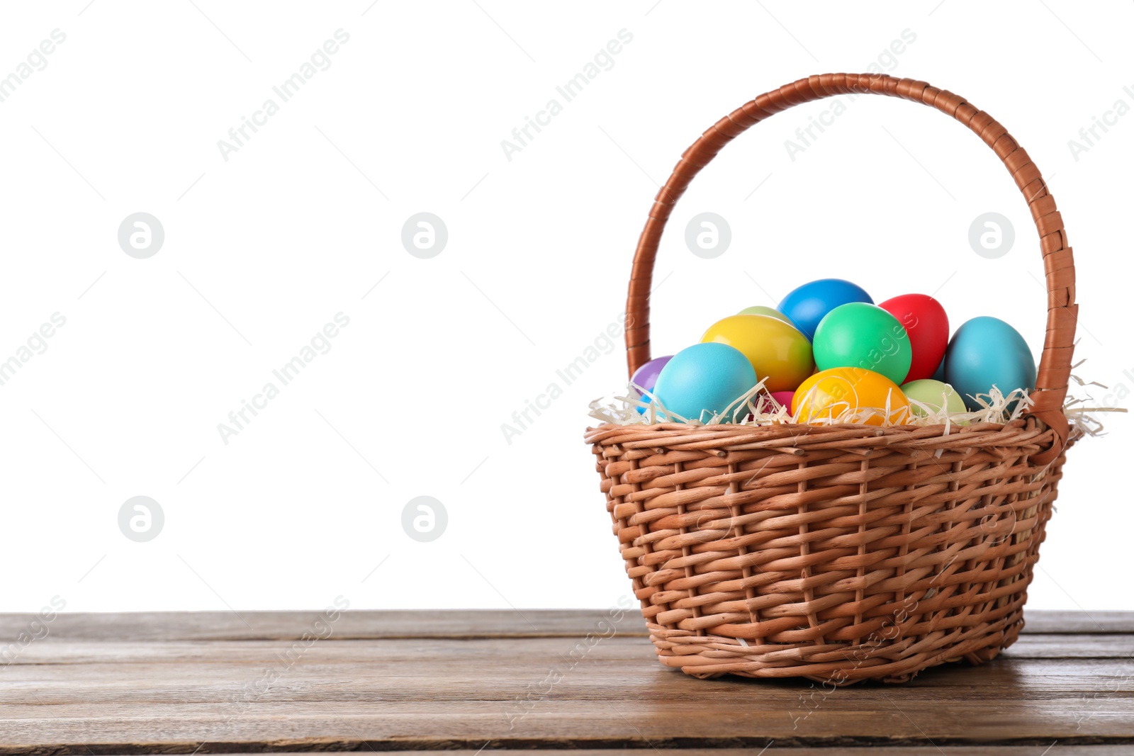 Photo of Colorful Easter eggs in wicker basket on wooden table against white background