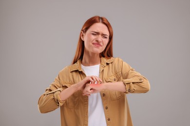 Suffering from allergy. Young woman scratching her arm on grey background