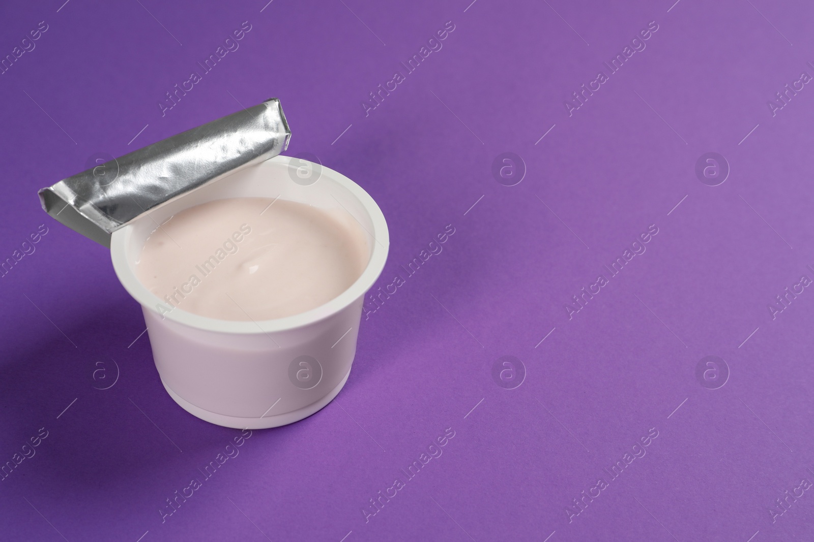 Photo of Plastic cup with tasty yogurt on purple background, space for text