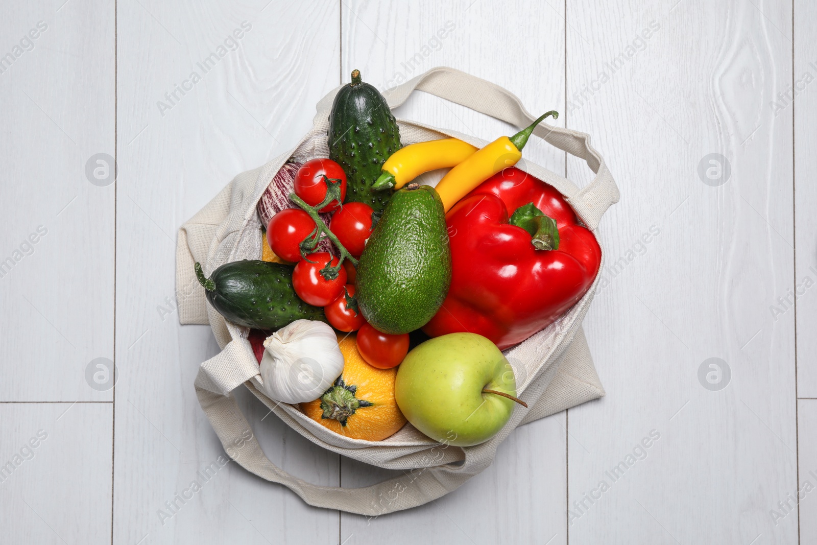 Photo of Bag full of fresh vegetables and fruits on light background, top view
