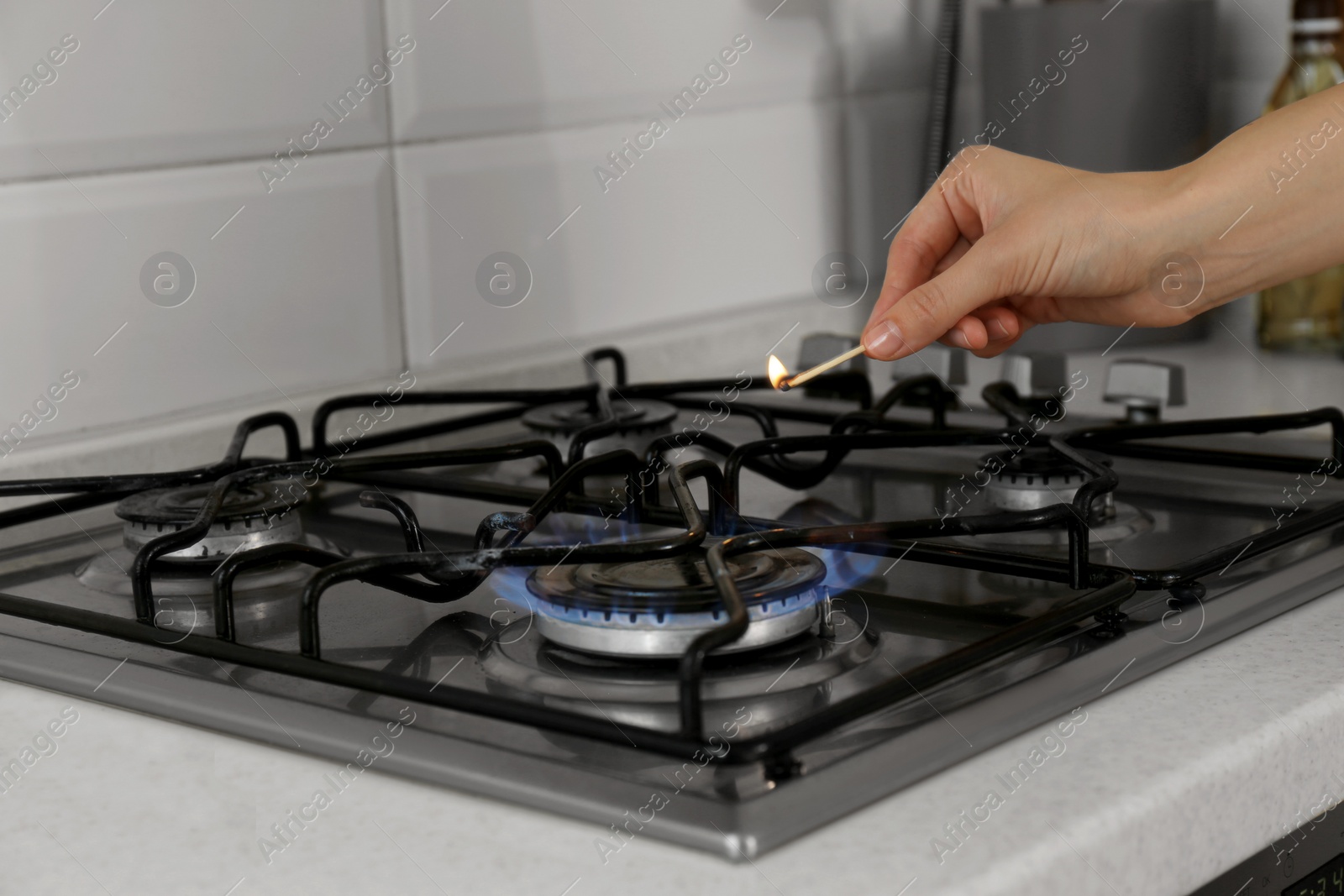 Photo of Woman lighting gas stove with match in kitchen, closeup