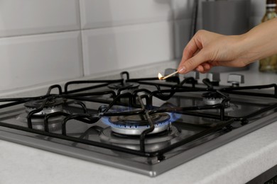 Photo of Woman lighting gas stove with match in kitchen, closeup
