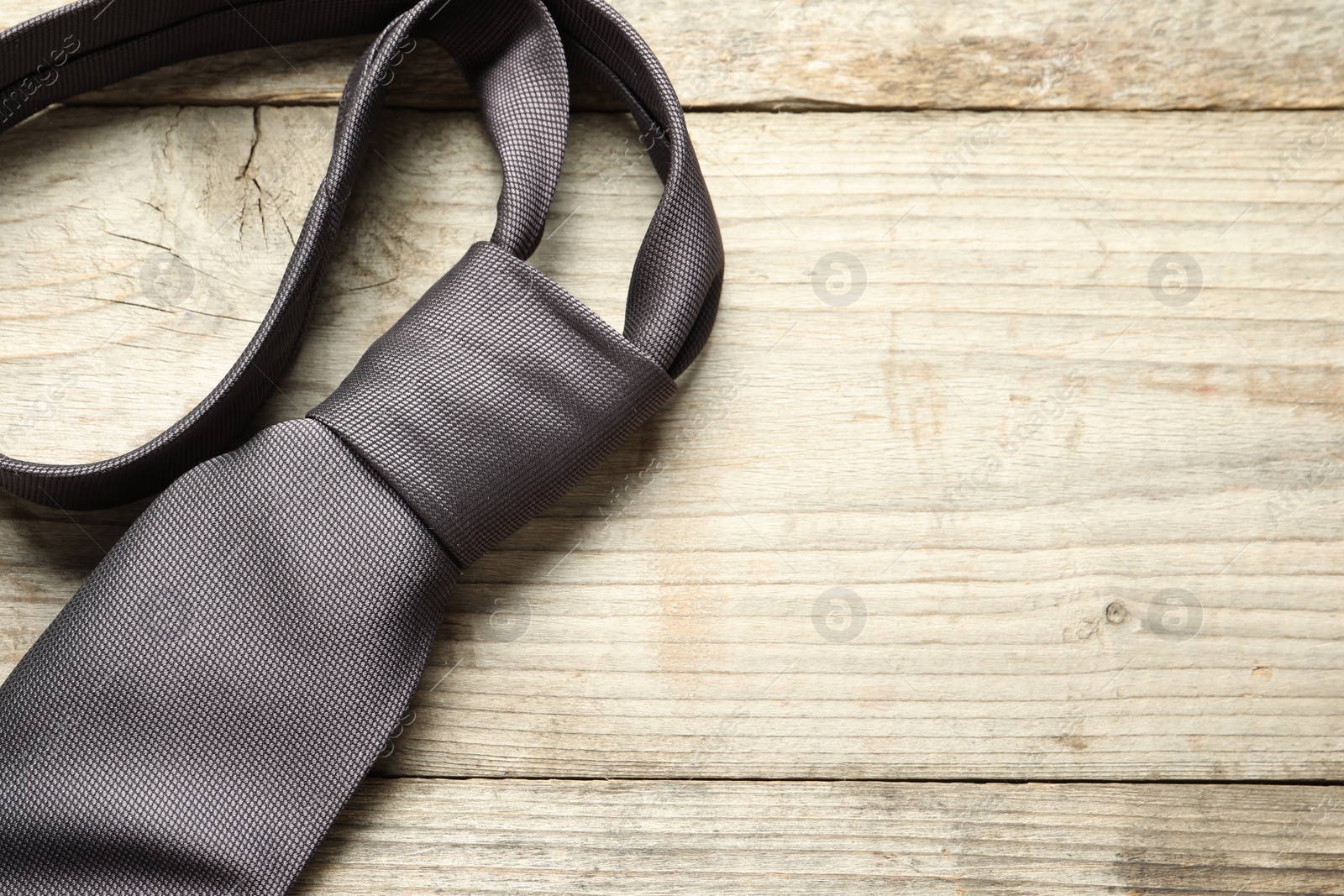 Photo of One necktie on light wooden table, above view. Space for text