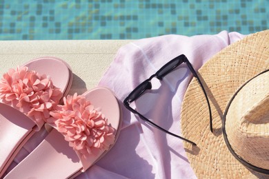 Pink blanket with slippers, hat and sunglasses near outdoor swimming pool on sunny day, flat lay