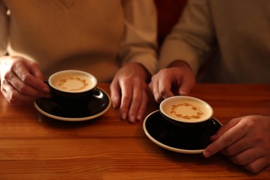 Photo of Couple with cups of aromatic coffee at wooden table, closeup