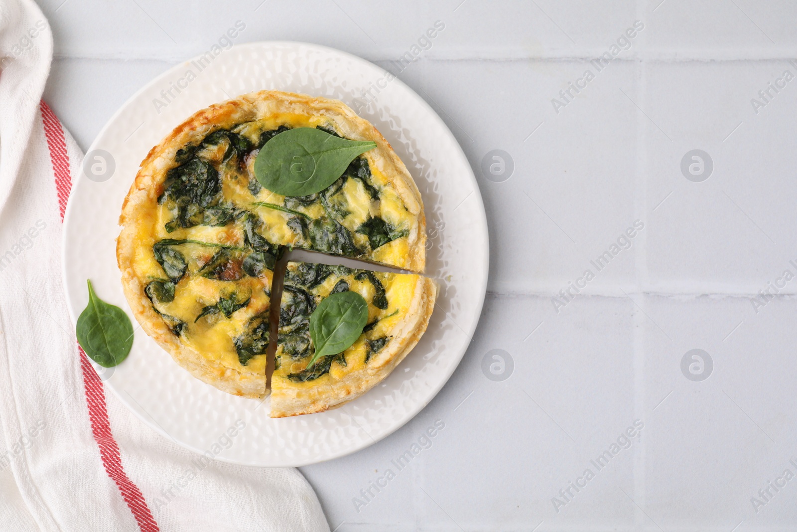 Photo of Delicious pie with spinach on white tiled table, top view. Space for text